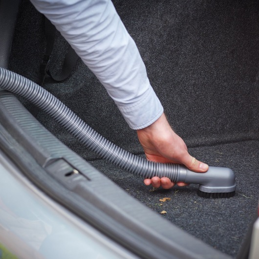 BLACKDECKER ADV1200 car vacuum in use cleaning vehicle trunk carpet with flexible hose attachment.