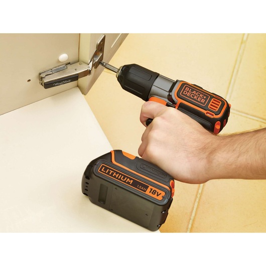 BLACK+DECKER ASD18KB cordless drill used to fasten a hinge, black and orange, close-up photo.