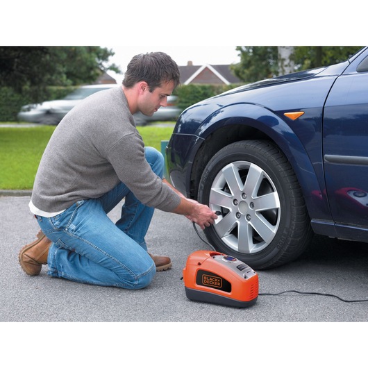 Photo of BLACKDECKER ASI300 portable inflator being used to inflate a car tire outdoors.