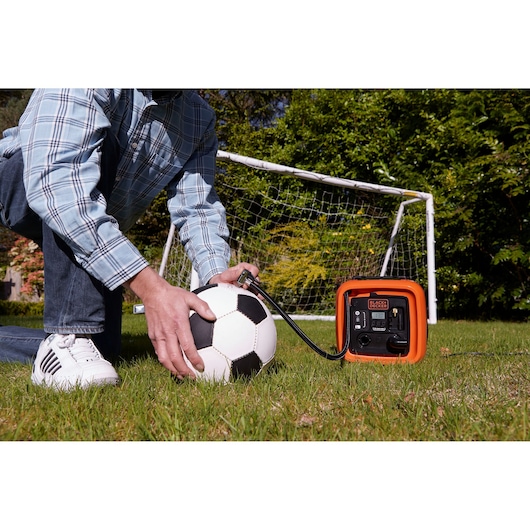BLACKDECKER ASI400 portable air compressor inflating soccer ball on grass near goal post.
