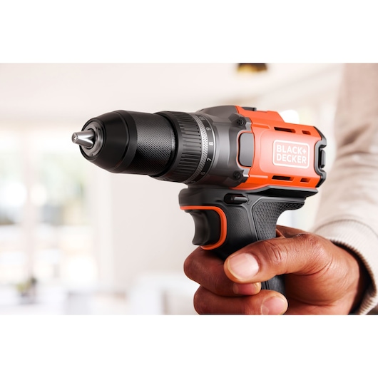 Hand holding a BLACK+DECKER cordless drill in an indoor setting, close-up view of the tool.