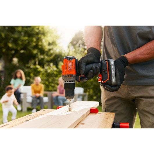 Photo of BLACKDECKER BCD383D1 cordless drill in use on wood, outdoors, person wearing gloves.