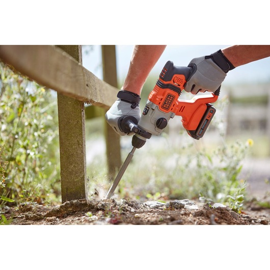 BLACKDECKER BCD900B cordless rotary hammer drill with chisel bit, used outdoors near a wooden post.