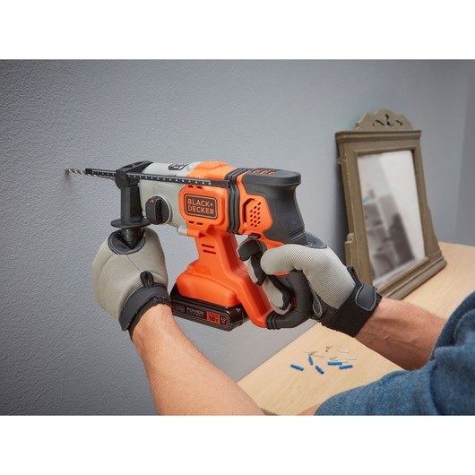 BLACK+DECKER BCD900B cordless hammer drill in use on a wall, close-up side view, operator wearing gloves.