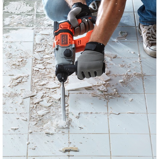 BLACK+DECKER BCD900D1S rotary hammer used to remove tiles on a white tiled floor, close-up view.