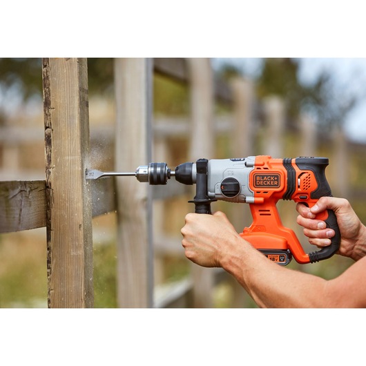 BLACK+DECKER BCD900D1S cordless hammer drill in use, drilling into outdoor wooden post.