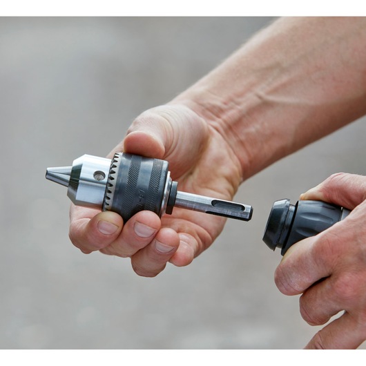 Close-up of hands attaching BLACKDECKER BCD900D1S drill chuck accessory outdoors.