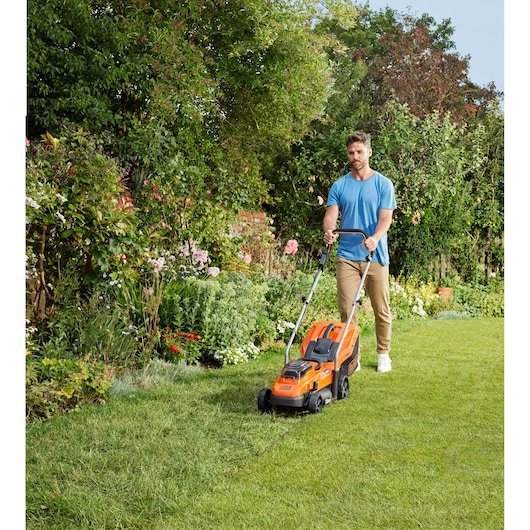 BLACKDECKER BCMW33184L2 cordless lawn mower in use on green grass in a garden setting.