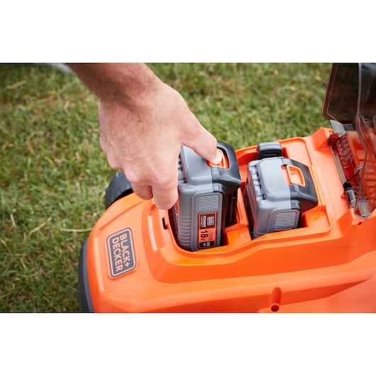 BLACK+DECKER BCMW33184L2 lawn mower close-up of hand inserting 18V battery into orange battery compartment.