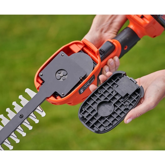 Photo of BLACK+DECKER BCSS18D1 handheld shrub shear with battery cover removed, showing internal mechanism, outdoors.
