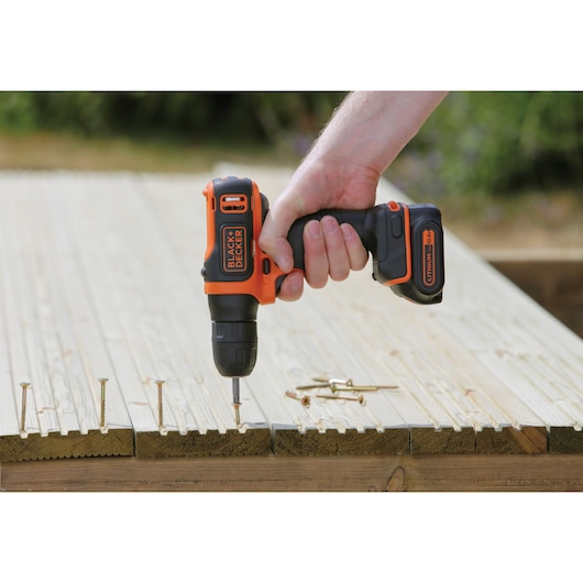 BLACK+DECKER BDCD12 cordless drill used by hand to drive a screw into wooden board outdoors.