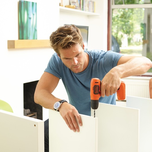 Photo of BLACKDECKER BDCD8K cordless drill in use for assembling white furniture indoors.