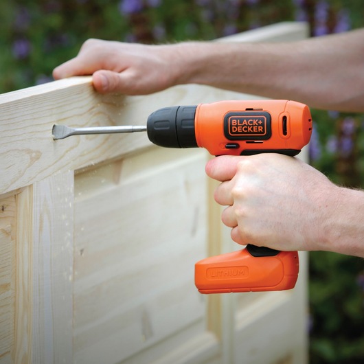 Photo of BLACK+DECKER BDCD8K orange cordless drill in use on light wood.