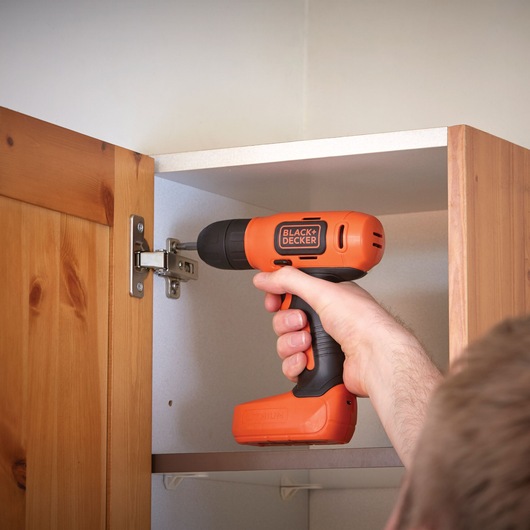 Photo of BLACK+DECKER BDCD8K cordless drill in use on cabinet hinge indoors.