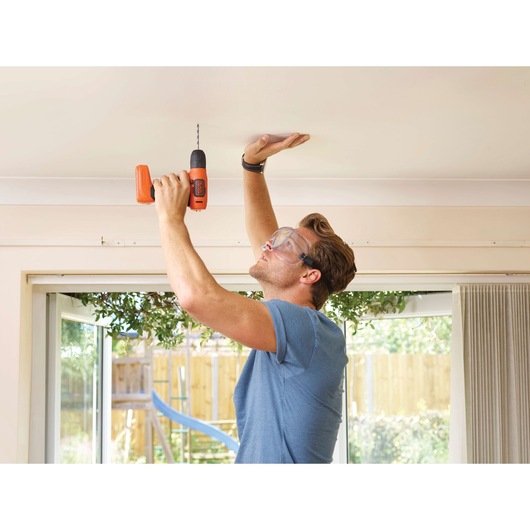 Photo of BLACKDECKER BDCD8 cordless drill being used to drill into a ceiling indoors.
