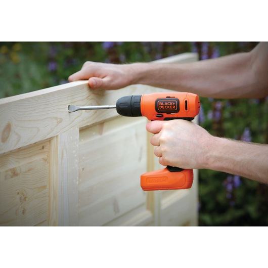Photo of BLACKDECKER BDCD8 cordless drill being used on light wood panel outdoors.