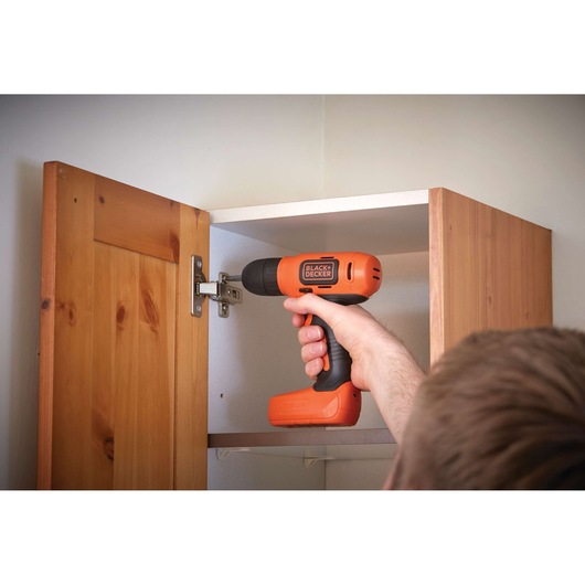 Photo of BLACKDECKER BDCD8 cordless drill being used to fix a cabinet hinge inside a wooden cupboard.