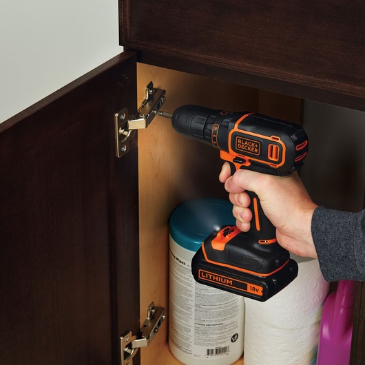 Photo of BLACKDECKER BDCDC18K1 cordless drill being used to tighten a hinge inside a wooden cabinet.
