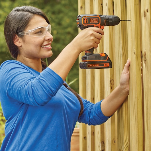 Photo of BLACKDECKER BDCDC18KB cordless drill in use, drilling into light wood outdoors.