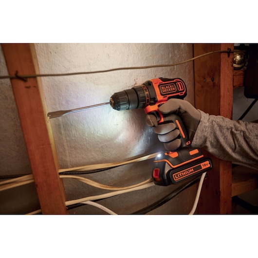 BLACK+DECKER BDCDD186K cordless drill with 18V lithium battery in use on a wall, user wearing gloves.
