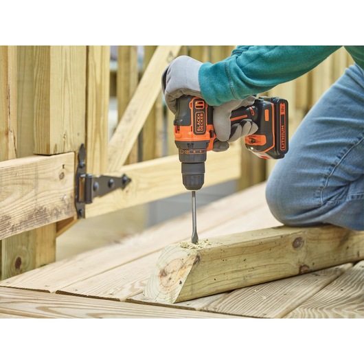 BLACKDECKER BDCDD186 cordless drill being used to drill wood outdoors, close-up of tool and user's hand.