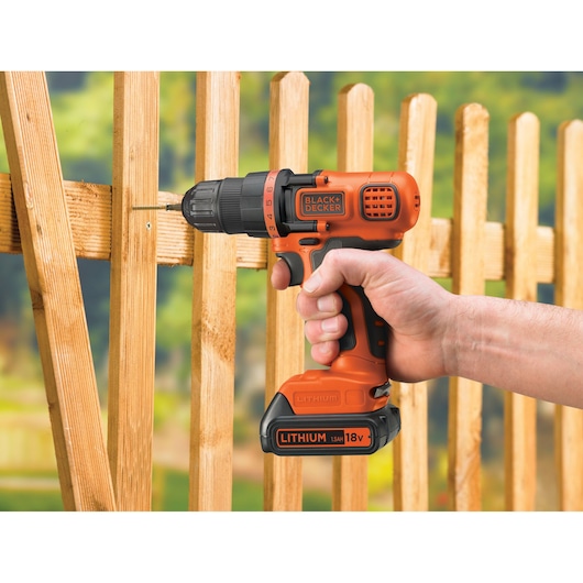 BLACKDECKER BDCDD18N cordless drill driving a screw into a wooden fence, outdoor setting.