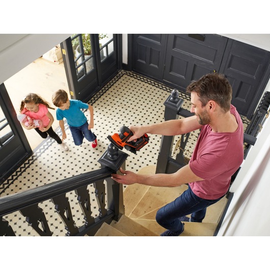 BLACK+DECKER BDCDS18 cordless sander being used on a black staircase handrail in a home interior.