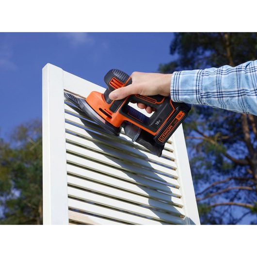 Photo of BLACK+DECKER BDCDS18 cordless sander in use on white shutters, outdoors.