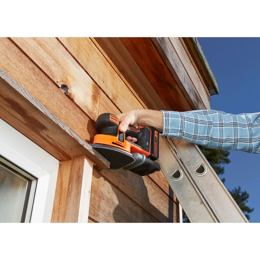 Photo of BLACKDECKER BDCDS18 cordless sander in use on wooden siding outdoors.
