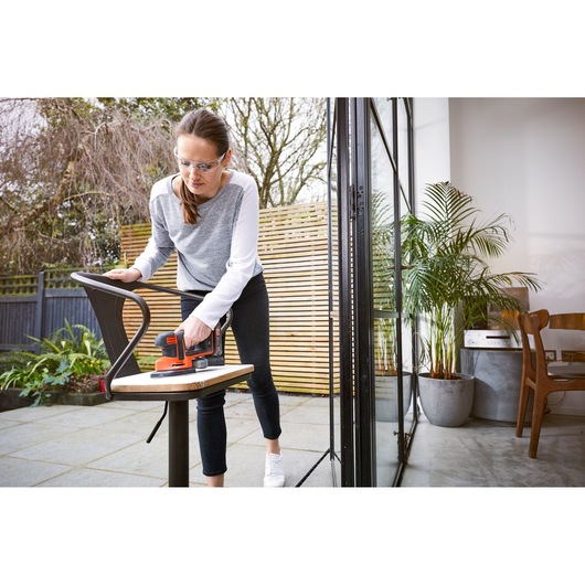 BLACKDECKER BDCDS18 sander used on a chair outdoors, person holding tool near patio door.