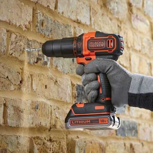 BLACK+DECKER BDCHD18K1B2 cordless drill in use drilling into a brick wall, close-up view.