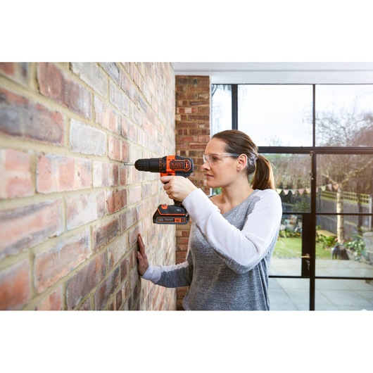 BLACKDECKER BDCHD18K1B2 cordless drill being used on a brick wall indoors, photography product category.