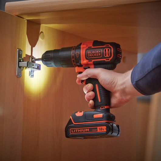 BLACKDECKER BDCHD18KB cordless drill being used to install a cabinet hinge, 18V lithium battery visible.