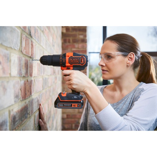 Photo of a person using a BLACK+DECKER BDCHD18KST cordless drill to drill into a brick wall indoors.