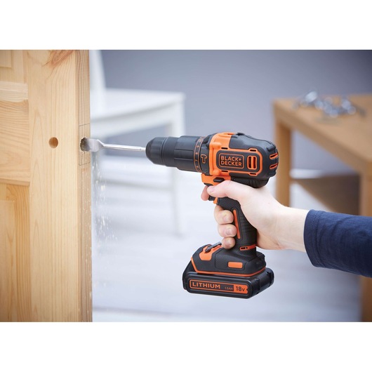 Photo of BLACKDECKER BDCHD18 cordless drill in use drilling into light wood, visible 18V lithium battery.