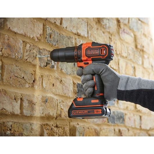 BLACK+DECKER BDCHD18 cordless drill in use on brick wall, orange and black color, photography close-up.