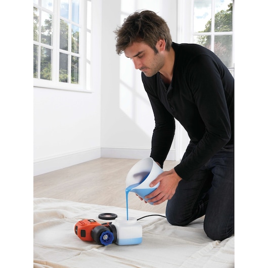 BLACKDECKER BDPS200 paint sprayer on floor, person pouring blue paint into container, indoor setting.