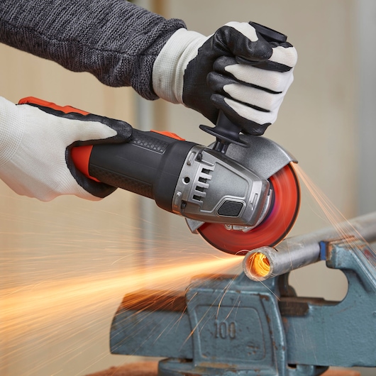 BLACKDECKER BEG220A6 angle grinder cutting metal pipe, close-up with sparks flying.