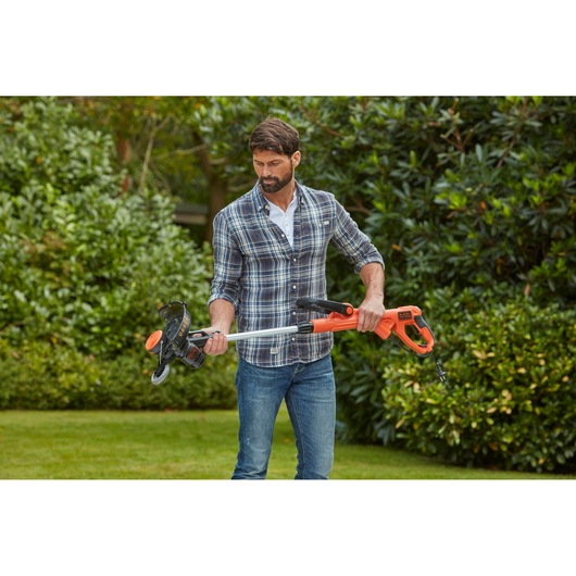Person holding BLACKDECKER BESTE630CM orange and black grass trimmer in a garden.
