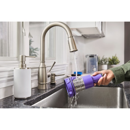 Person rinsing the BLACK+DECKER BHFEA640WG vacuum filter under a kitchen faucet in a modern kitchen.