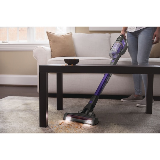 BLACKDECKER BHFEV182CP stick vacuum cleaning crumbs on carpet near table in living room.