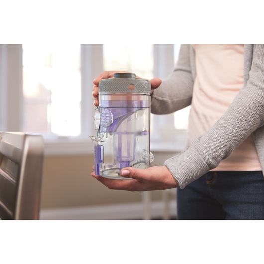 Photo of person holding BLACKDECKER BHFEV182CP vacuum dust canister with transparent purple components indoors.