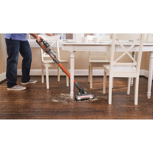 Photo of BLACK+DECKER BHFEV182C cordless stick vacuum cleaning debris from a dark wood floor under a dining table.