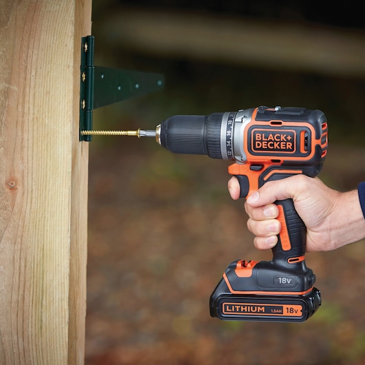 BLACK+DECKER cordless drill BL186KB held, driving screw into wooden post outdoors.