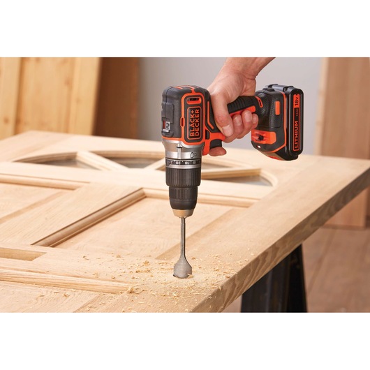 BLACK+DECKER BL188K cordless drill in use on wooden door, close-up view, orange and black design.