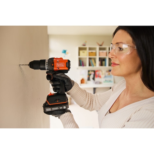 Photo of a person using a BLACK+DECKER BLD683XN cordless drill on a wall indoors.