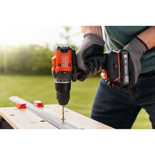 Photo of BLACK+DECKER BLD683XN cordless drill in use, drilling into metal bar, user wearing gloves outdoors.