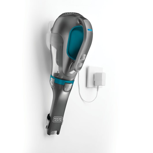 A BLACK+DECKER handheld vacuum cleaner model DV1210N mounted on a wall with its charging adapter plugged into an outlet.