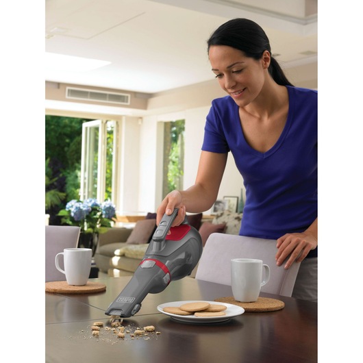 BLACKDECKER DV1415EL handheld vacuum cleaning crumbs on table near mugs and plate of cookies in kitchen.