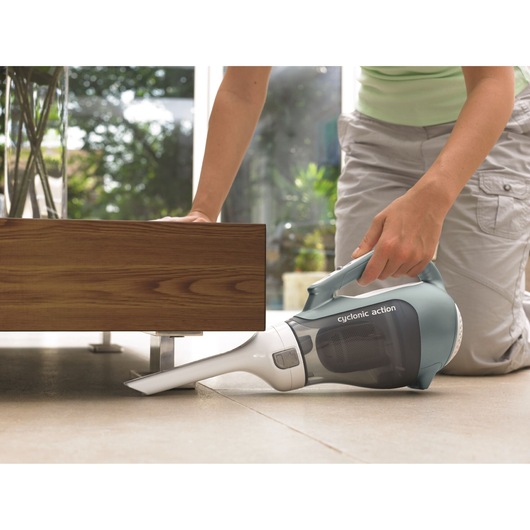 Photo of BLACK+DECKER DV7210ECN handheld vacuum cleaner with gray and white body, cleaning under wooden furniture.
